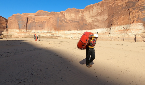 Photo by Tom Unger.  Brad Mitchell carrying his packraft as we portage a large river bend_where the Escalante River runs into Lake Powel.png